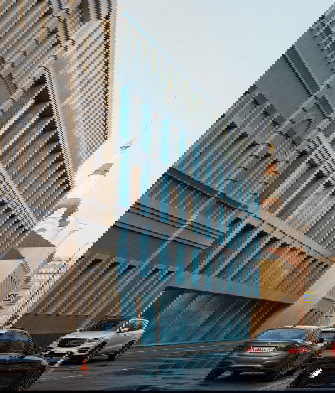 Вид по диагонали на синий фасад клуба на Балчуге: стык современной облицовки и исторической застройки, автомобили и городской пейзаж с церковной башней на заднем плане.