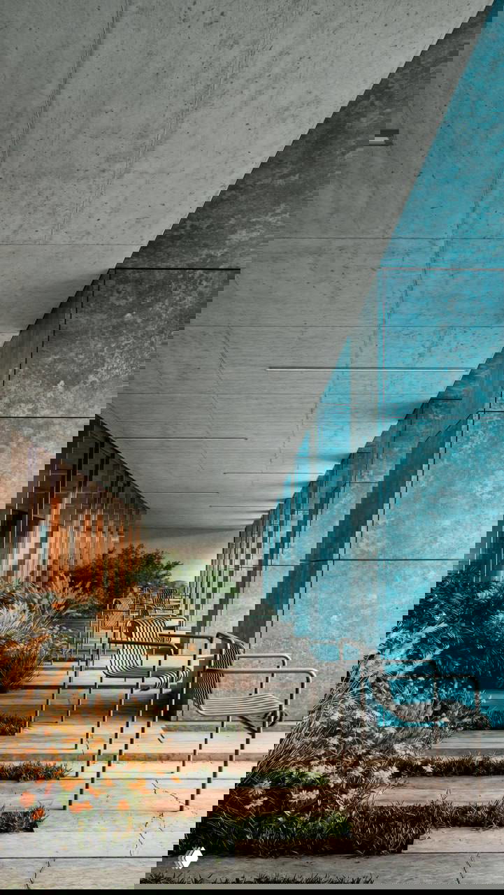 Интерьерная визуализация галереи: бетонный потолок, синие колонны из крупноформатного титана, террасы с растительностью и металлические стулья вдоль фасада.