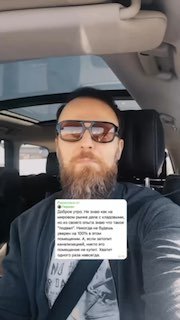 Кадр из вертикального видео: мужчина в салоне автомобиля в солнцезащитных очках держит листок с текстом; контекст — пояснение рисков затопления подвала.