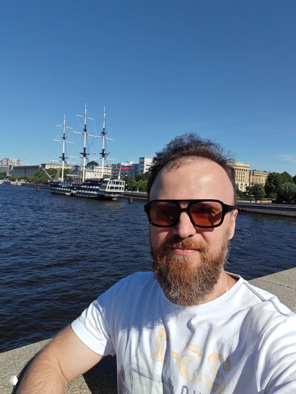 Селфи на набережной Невы в Санкт-Петербурге: на фоне причаленный парусник, набережная и исторические здания центральной части города.
