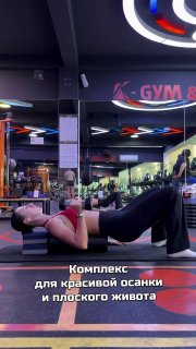 Женщина в спортзале лежит на спине, выполняет упражнения для передней зубчатой и поперечной мышцы на коврике, вид общий.