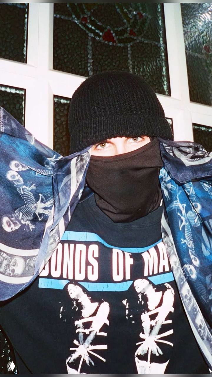 Человек в тёмной вязаной шапке и маске, видны только глаза; шарф с узором и футболка с принтом, снимок в помещении, крупный план