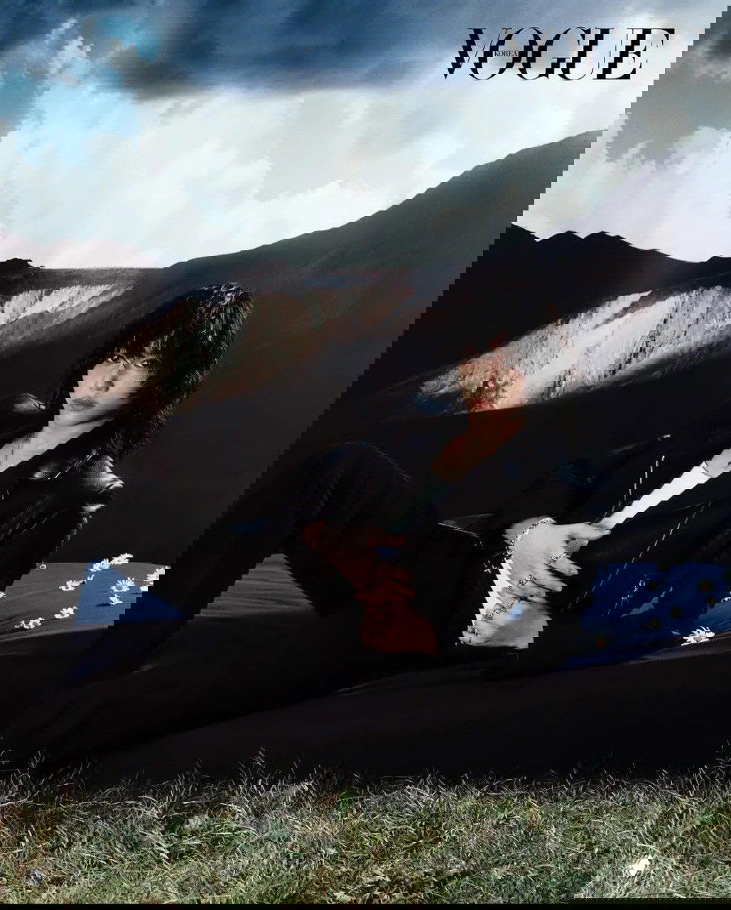 Модель лежит на фоне пейзажа в кадре Vogue Korea: черная кожаная куртка, расслабленная поза и журнальная эстетика в природе.