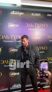 Джин Яман на красной ковровой дорожке в Москве у баннера премьеры: актёр позирует перед фотографами и смартфонами зрителей на фоне логотипов.