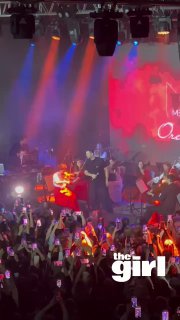 Вертикальное видео с концерта: артист и гитарист на сцене, разноцветная подсветка, толпа фанатов с поднятыми смартфонами.