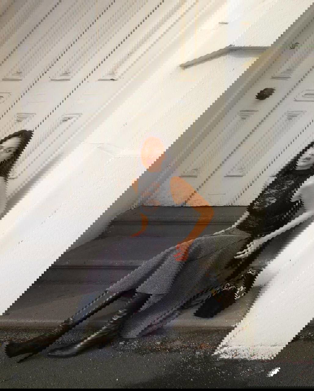 Девушка сидит на ступеньках в тёмном кружевном топе и юбке, образ сочетает уличную простоту и готические детали — тихая, меланхоличная поза.