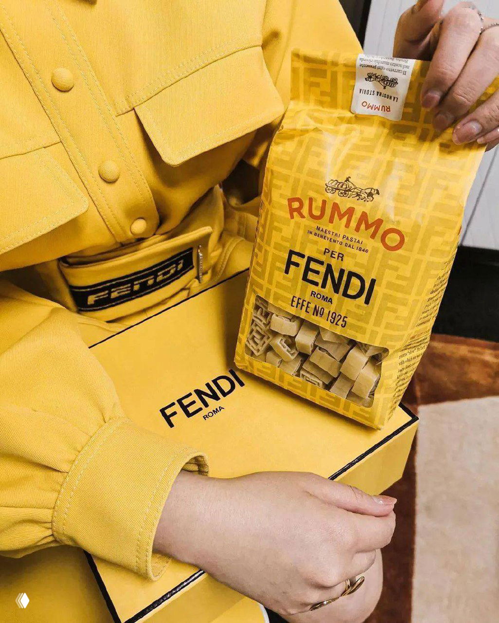 Пакет макарон Rummo с буквенным монограммным рисунком для Fendi: макароны и желтая упаковка рядом с коробкой и одеждой бренда на фотографии.