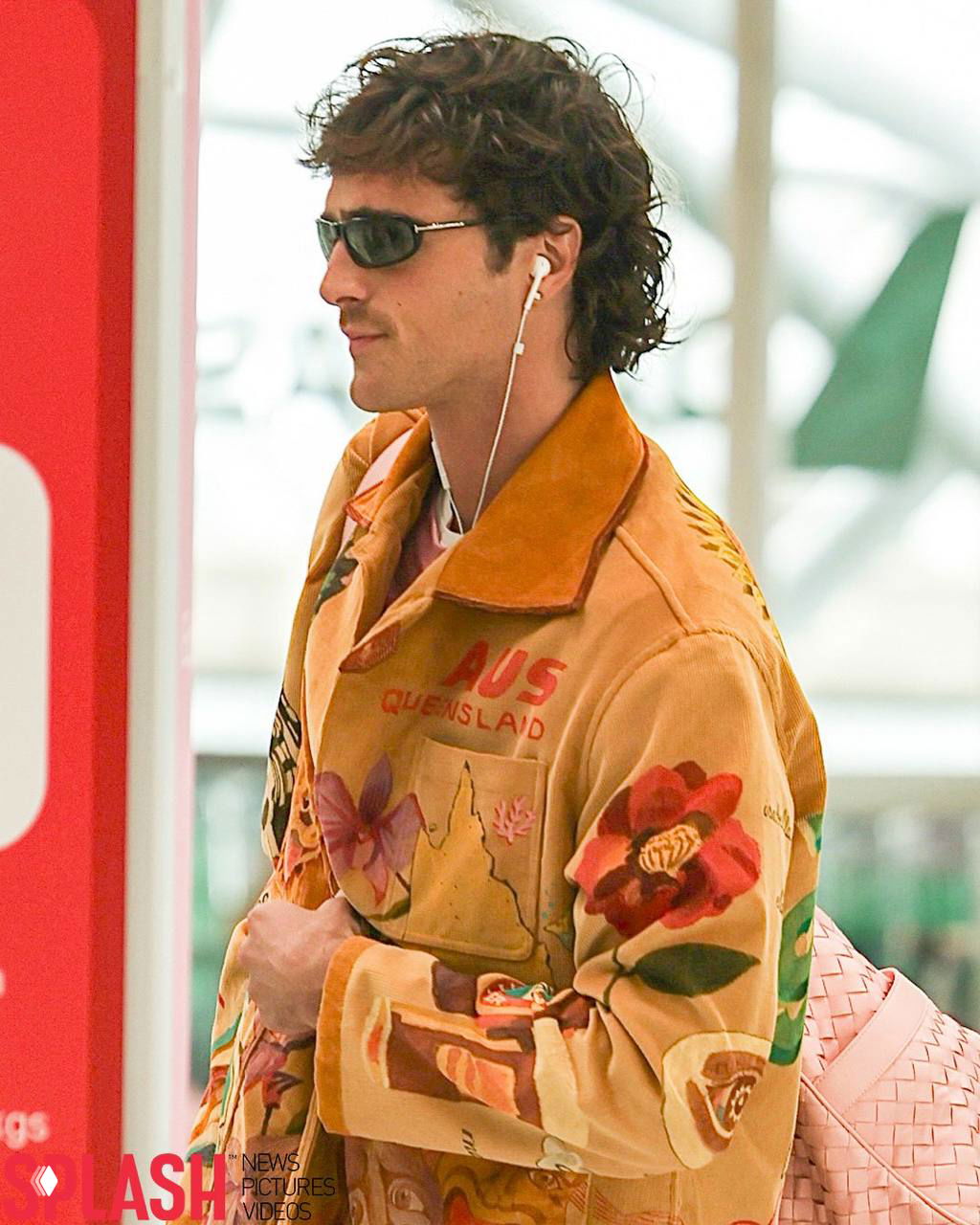 Портрет в профиль: мужчина в солнечных очках, с белыми проводными наушниками и вниманием в сторону — фон размытый, интерьер аэропорта