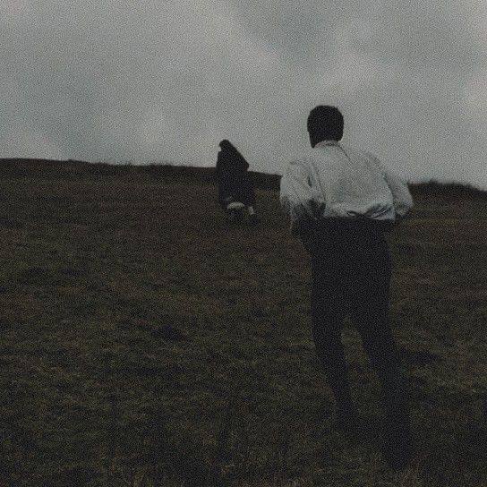 Зернистый чёрно-белый кадр с двумя фигурами, бегущими по холму — кинематографическая сцена с драматическим настроением в духе «Грозовой перевал».