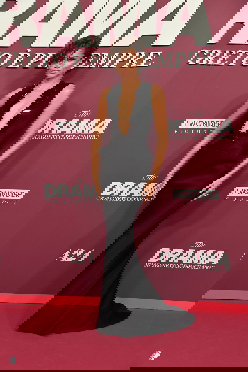 Зендея позирует в полном рост на красной дорожке в чёрном платье Armani Privé; видна дорожка и брендовые логотипы премьеры на фоне.