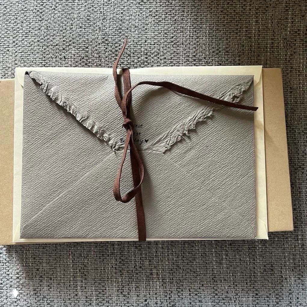 Пакет с конвертом, пергаментной бумагой и коричневой лентой на текстурной поверхности — деталь романтической эстетики переписки в духе «Грозовой перевал».