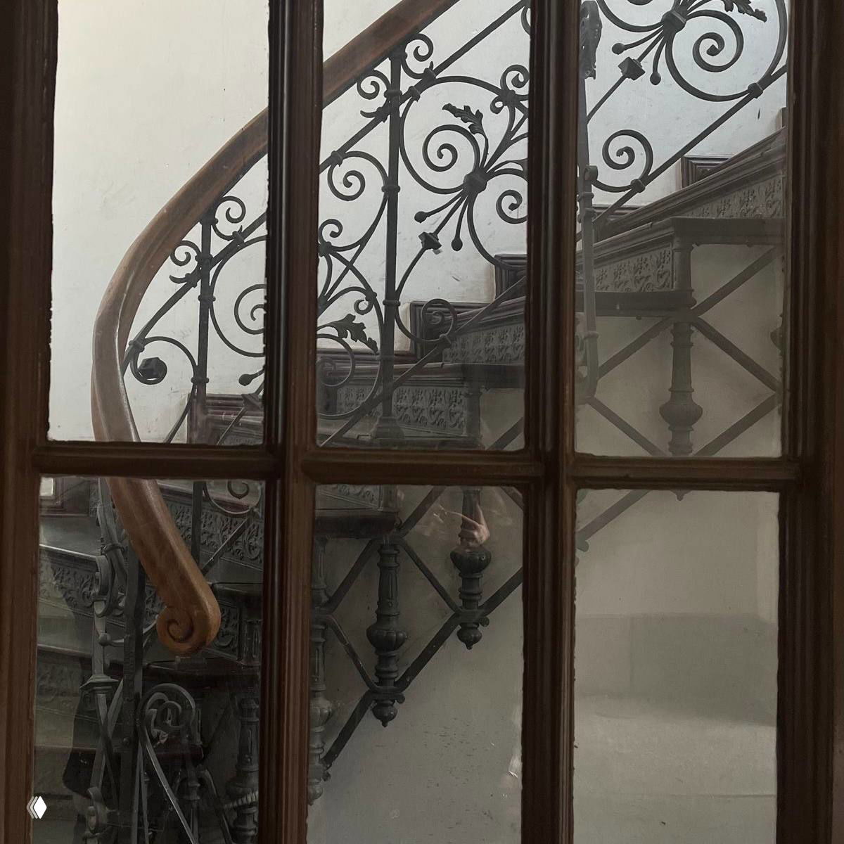 Кованая винтовая лестница, вид через оконную раму — интерьер старого дома с декоративным ограждением и патиной времени, в духе «Грозовой перевал».
