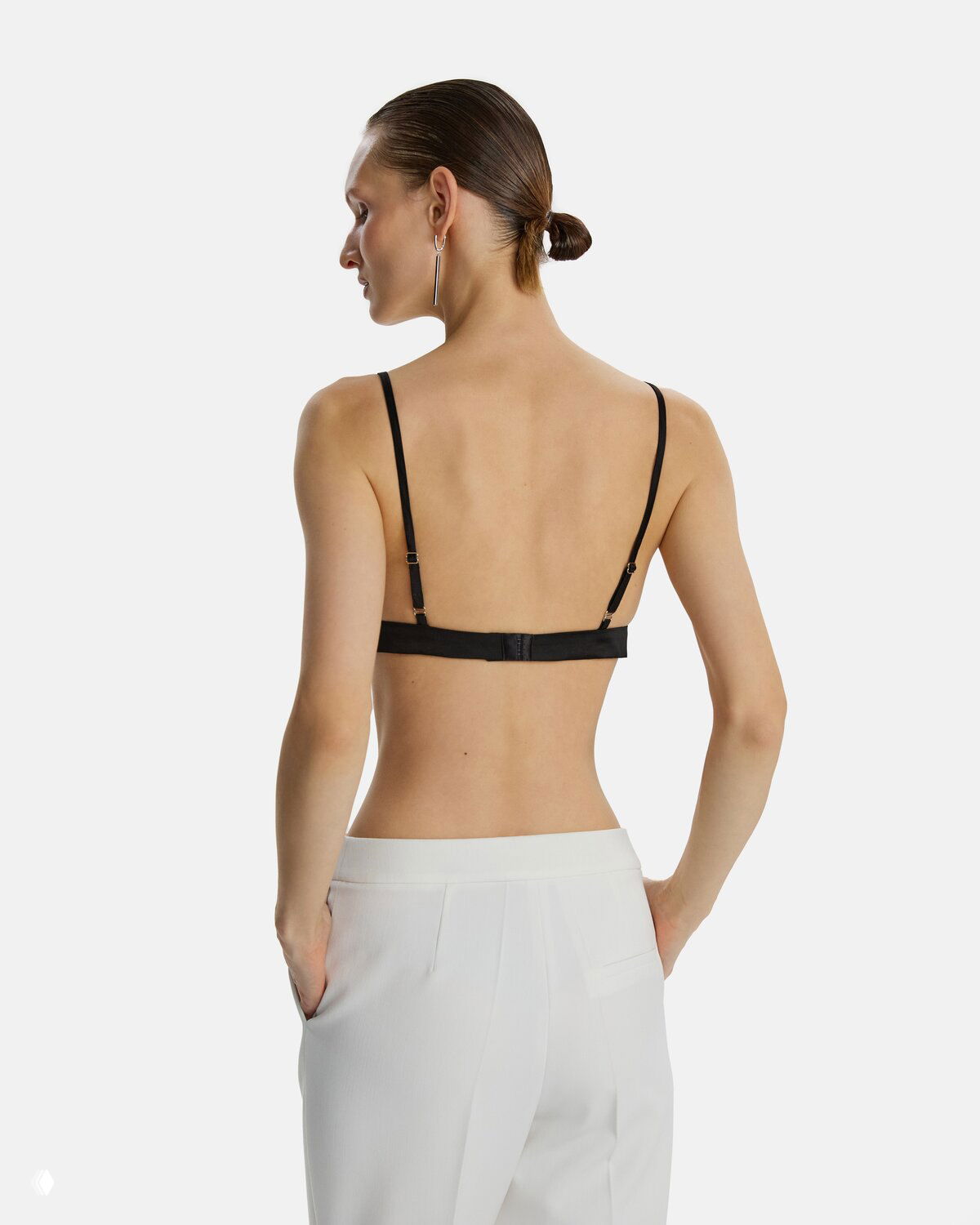 Тыльный вид модели в чёрном топе с открытой спиной и белых брюках, акцент на крое и посадке вещей из коллекции LIZURA 2025.