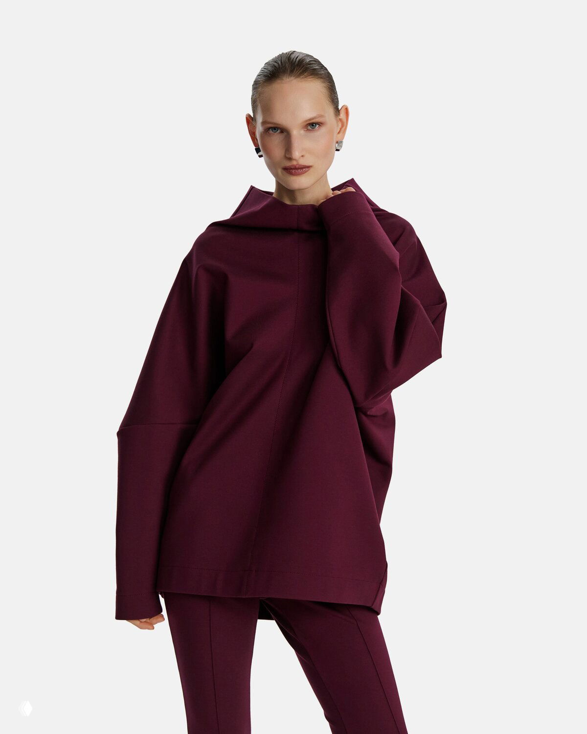Модель в бордовом худи и брюках — в коллекции есть и цвета, отличные от чёрного, но с той же сдержанной эстетикой и акцентом на форму.
