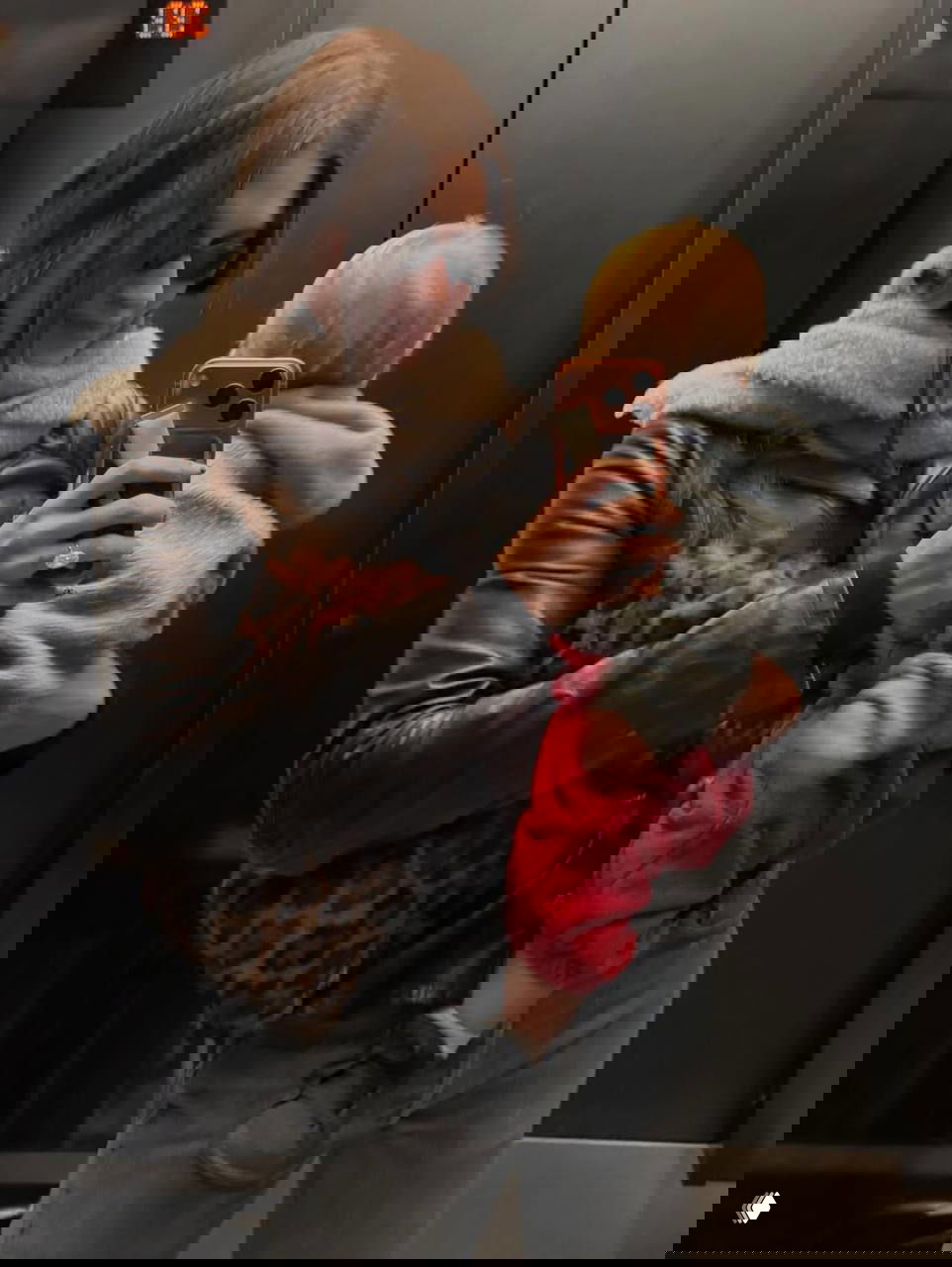 Зеркальное селфи в лифте: человек в кожаной куртке держит ребёнка, на переднем плане заметна леопардовая сумка и стильный образ с принтом.