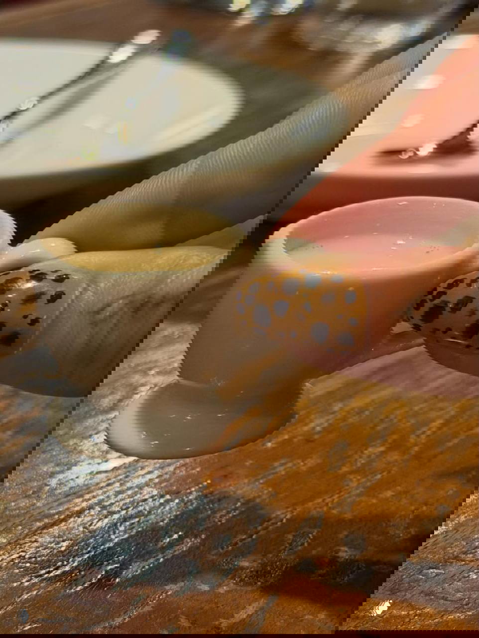 Крупный план пальца с необычным леопардовым маникюром: коричневая база и тёмные пятна на фоне деревянного стола и кофейной чашки.