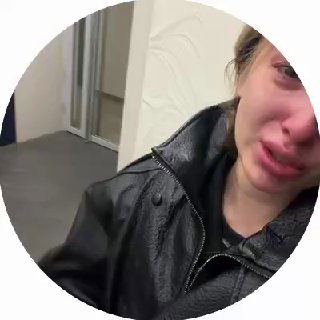 Круговой кадр: плачущая женщина у подъезда жилого комплекса, крупный план лица и плеч; видно слёзы, испуг и усталость после инцидента.