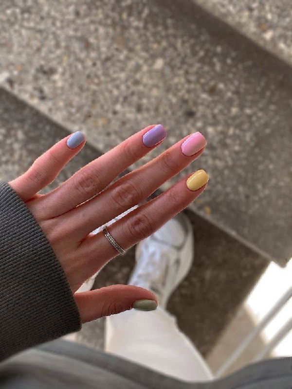 Пальцы с разноцветным пастельным маникюром: сиреневый, розовый, жёлтый и зелёный оттенки на повседневном фоне ступеней и кроссовок