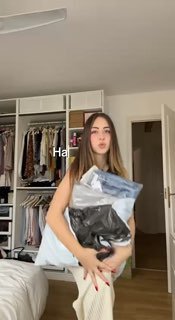 Кадр из видео: девушка в спальне собирает пакеты с одеждой и обсуждает покупки, показывая подбор вещей из подростковых/детских отделов для невысокого роста.