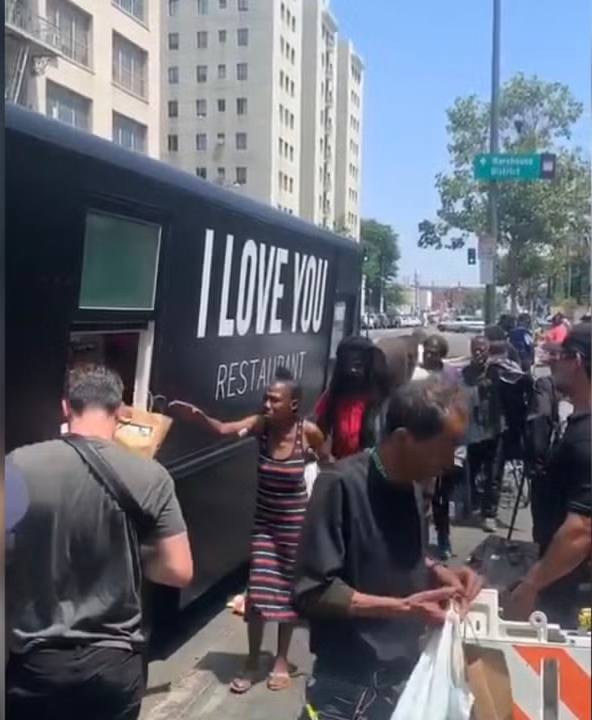 Уличный фуд‑трак с крупной надписью «I LOVE YOU», очередь людей и раздача еды на солнечной уличной сцене.