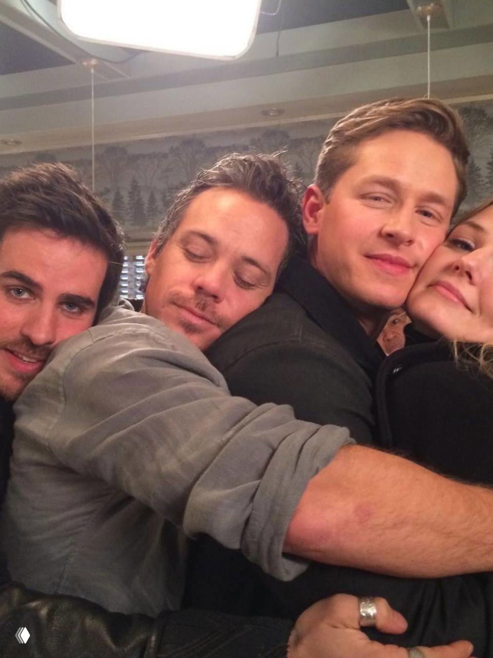 Групповой тёплый кадр: несколько человек обнимаются на фоне декора площадки, ощущается дружеская атмосфера за кадром.