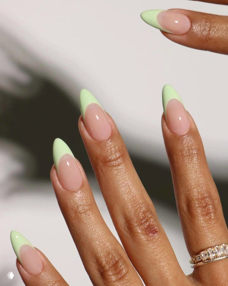 Пальцы тёмного тона кожи с заострёнными ногтями и пастельно-салатовым френчем; минималистичный дизайн на светлом фоне.