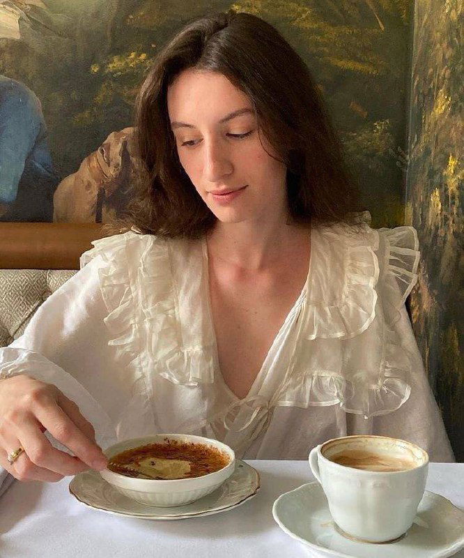 Портрет молодой женщины за столиком в кафе: белая блуза, чашка кофе и десерт на столе — интимная, спокойная эстетика poetcore.