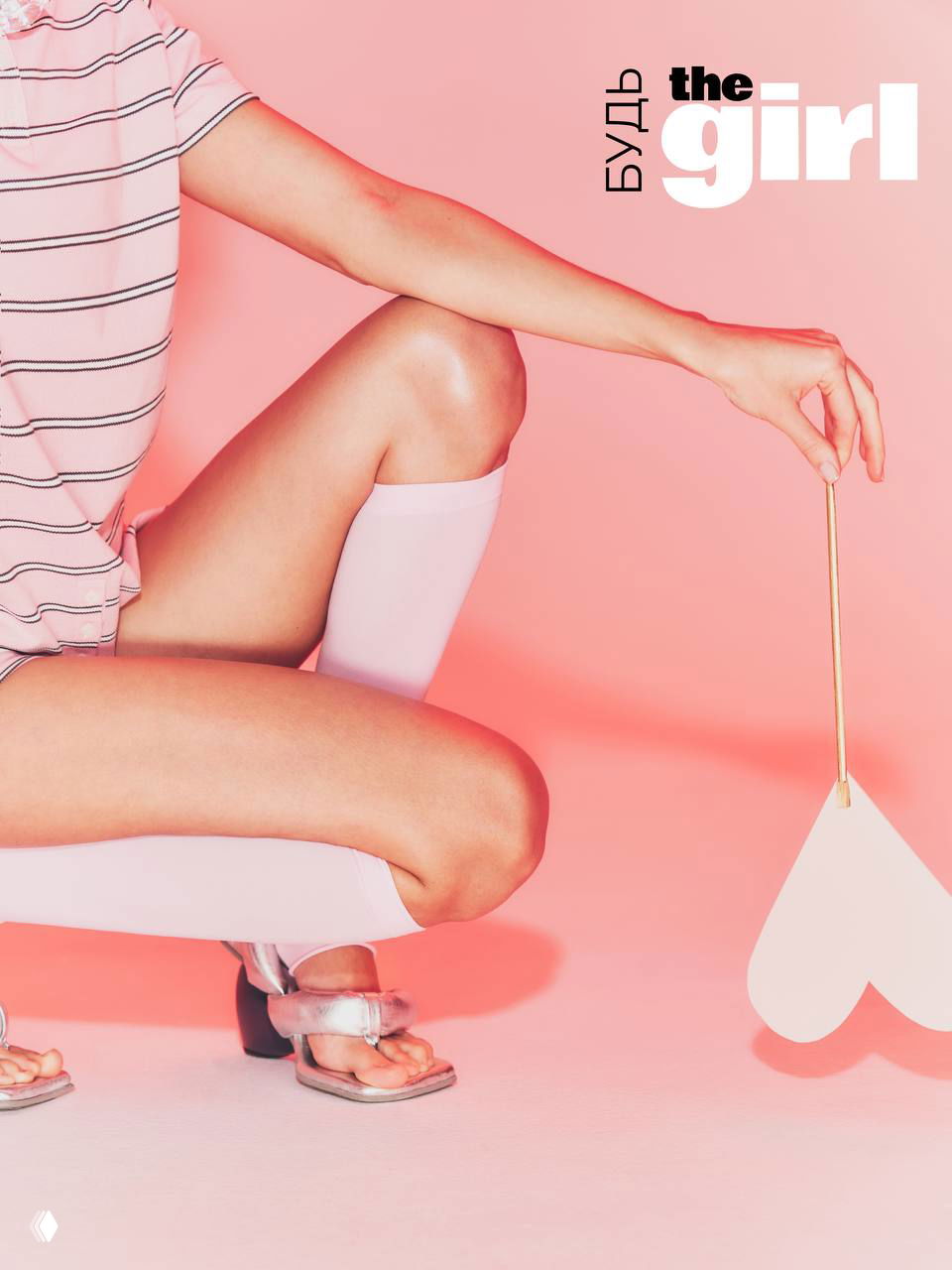 Кадр с присевшей моделью, акцент на ногах и сердечном реквизите на розовом фоне — стилизованная fashion-съёмка для кампании.