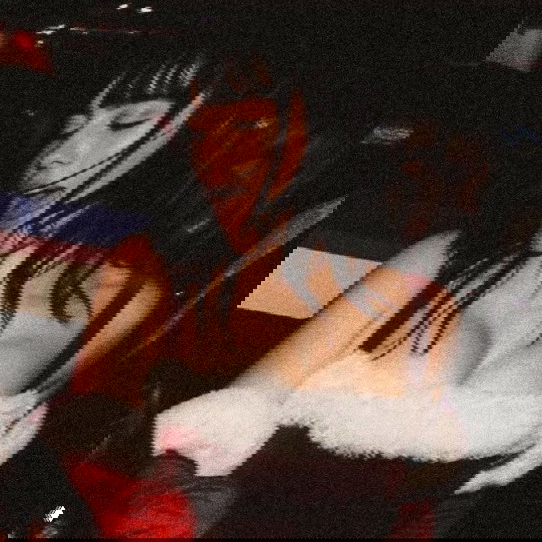 Праздничный портрет Билли Айлиш в красном костюме с пушистыми манжетами, расслабленное выражение лица и винтажная зернистость снимка.