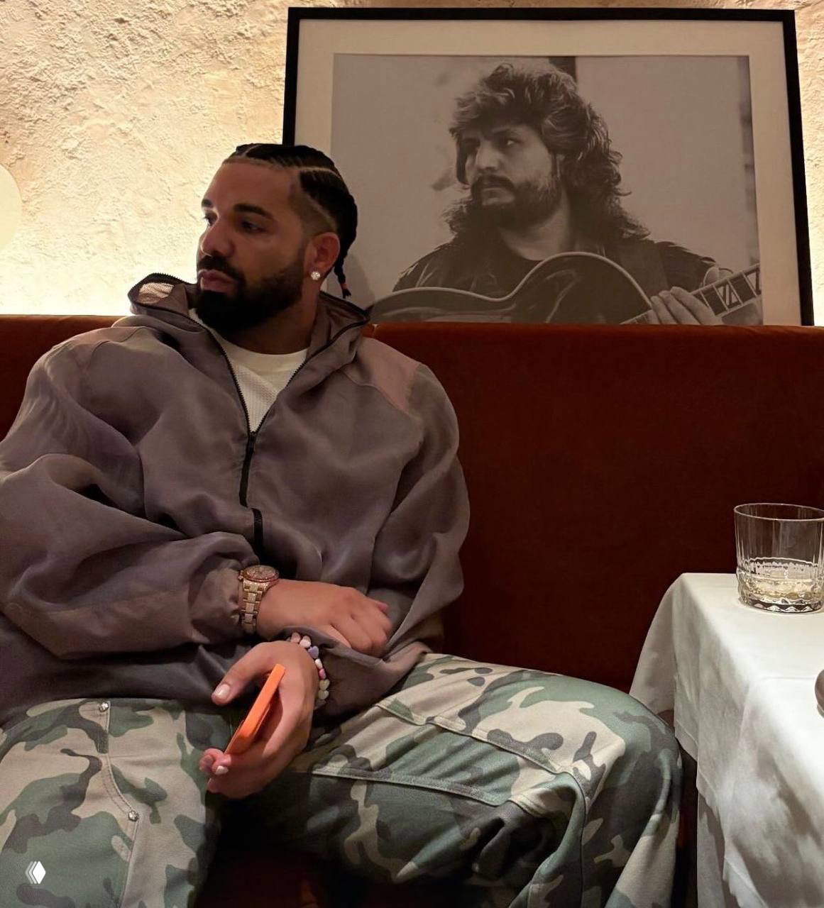 Дрейк сидит на диване в повседневной одежде, на стене позади крупная чёрно‑белая фотография музыканта — визуал для топ‑рэнкинга Spotify.