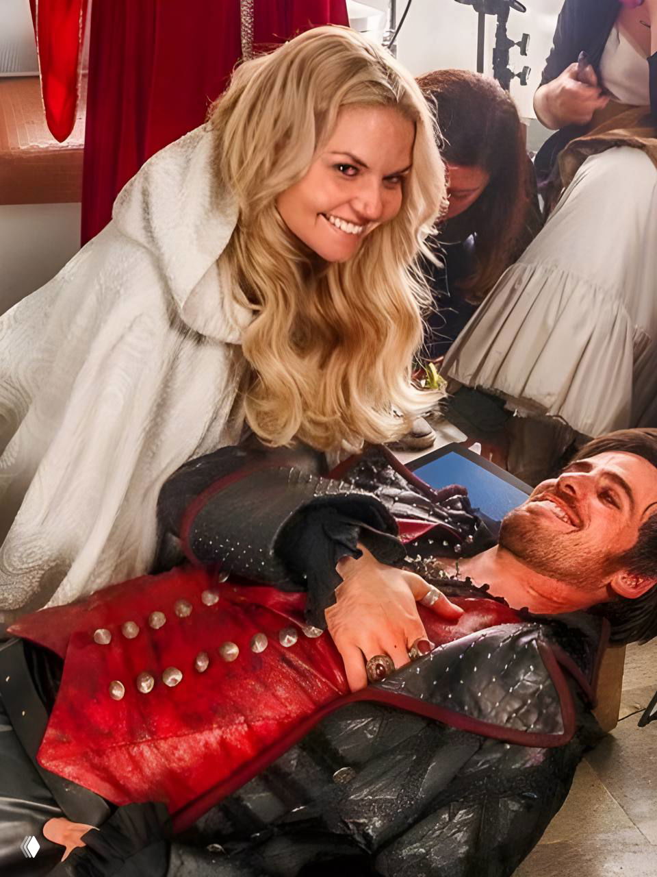 Яркая сценическая зарисовка: женщина в белом наклоняется над лежащим мужчиной в костюме, они улыбаются в постановочном кадре.