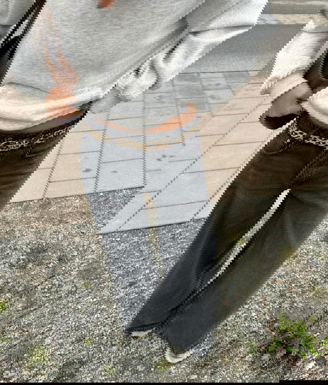 Человек в серой толстовке и чёрных широких джинсах, на поясе тонкий ремень в леопардовом принте — уличный образ в полный рост.