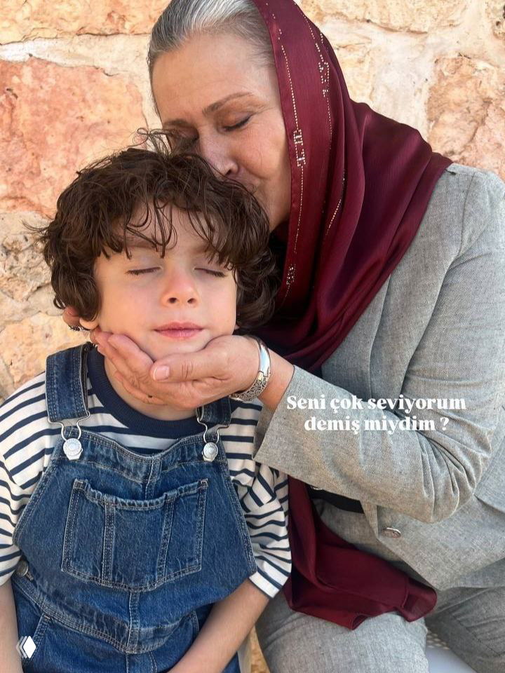 Актриса в платке обнимает и целует по щеке ребёнка в комбинезоне на фоне каменной стены — тёплый закадровый кадр со съёмок.