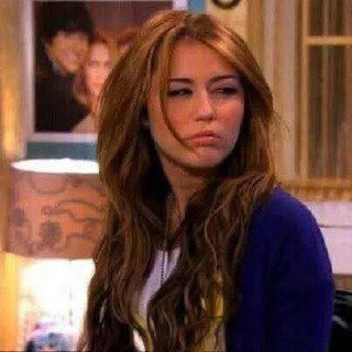 Крупный план персонажа из семейного ситкома: задумчивое лицо и мягкое домашнее освещение, интерьер с декоративными элементами на заднем плане.