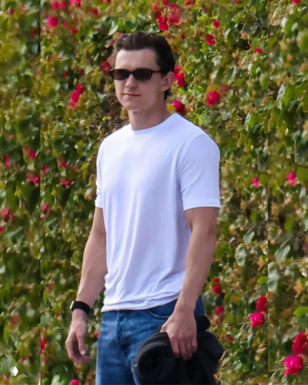 Мужчина в белой футболке и тёмных очках идёт по улице на фоне зелёной изгороди с цветами — полный рост, повседневный образ.