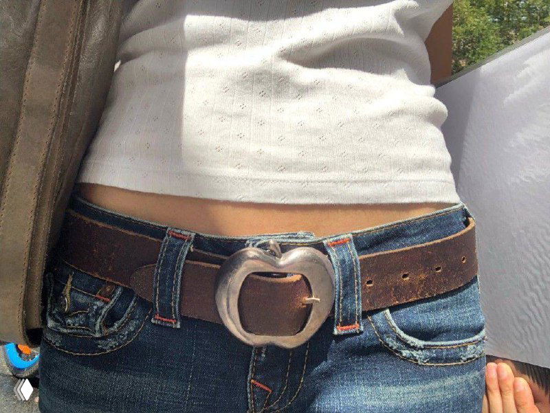 Поясная фотография в голубых джинсах с винтажным тёмно-коричневым ремнём и крупной округлой металлической пряжкой, солнечный свет.