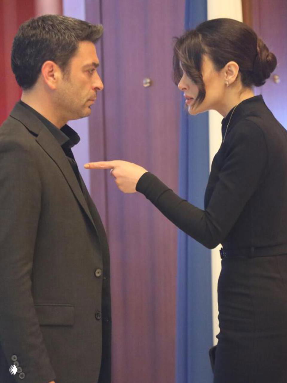 Интенсивный кадр из сериала: женщина указывает пальцем на мужчину в строгом костюме в коридоре, сцена конфликта между героями.