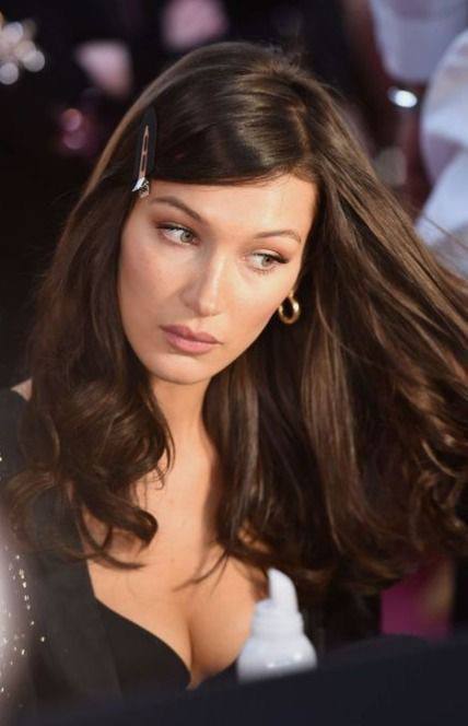 Крупный план женщины с тёмными волосами и боковой заколкой; мягкая челка, объёмные локоны и вечерний макияж.