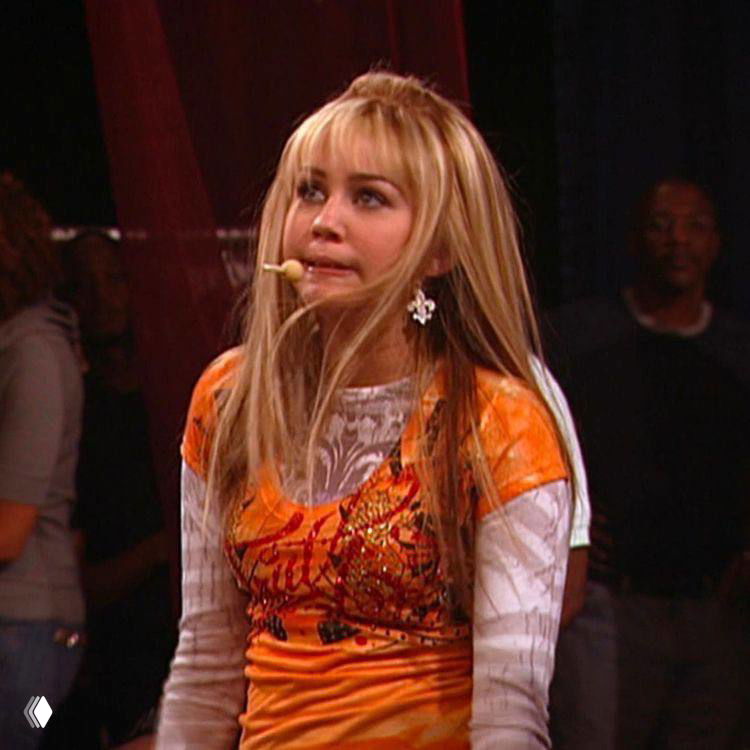 Сцена со сценическим образом персонажа: оранжевый костюм и микрофон-гарнитура, выражение лица перед выступлением в эпизоде шоу.