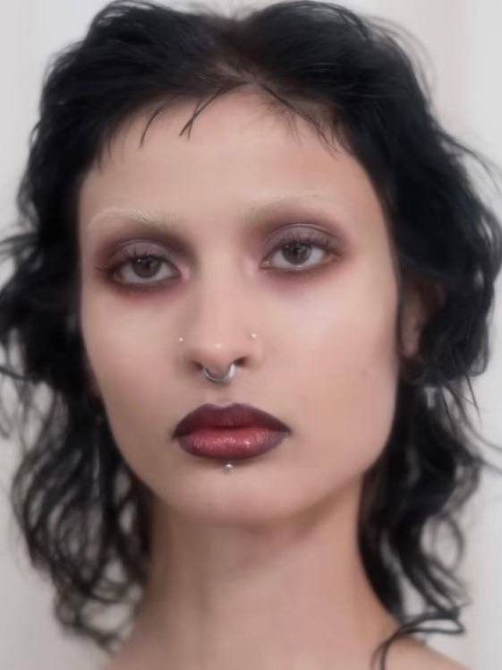 Портрет с тёмным дымчатым макияжем век в духе 90-х, матовые губы и пирсинг — контрастный бьюти‑образ с акцентом на глаза.