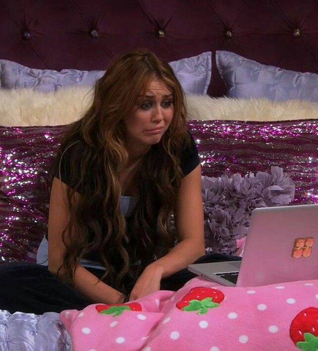 Сцена в спальне из ситкома: персонаж сидит за ноутбуком на кровати с розовым покрывалом, выражение задумчивости и лёгкой грусти.