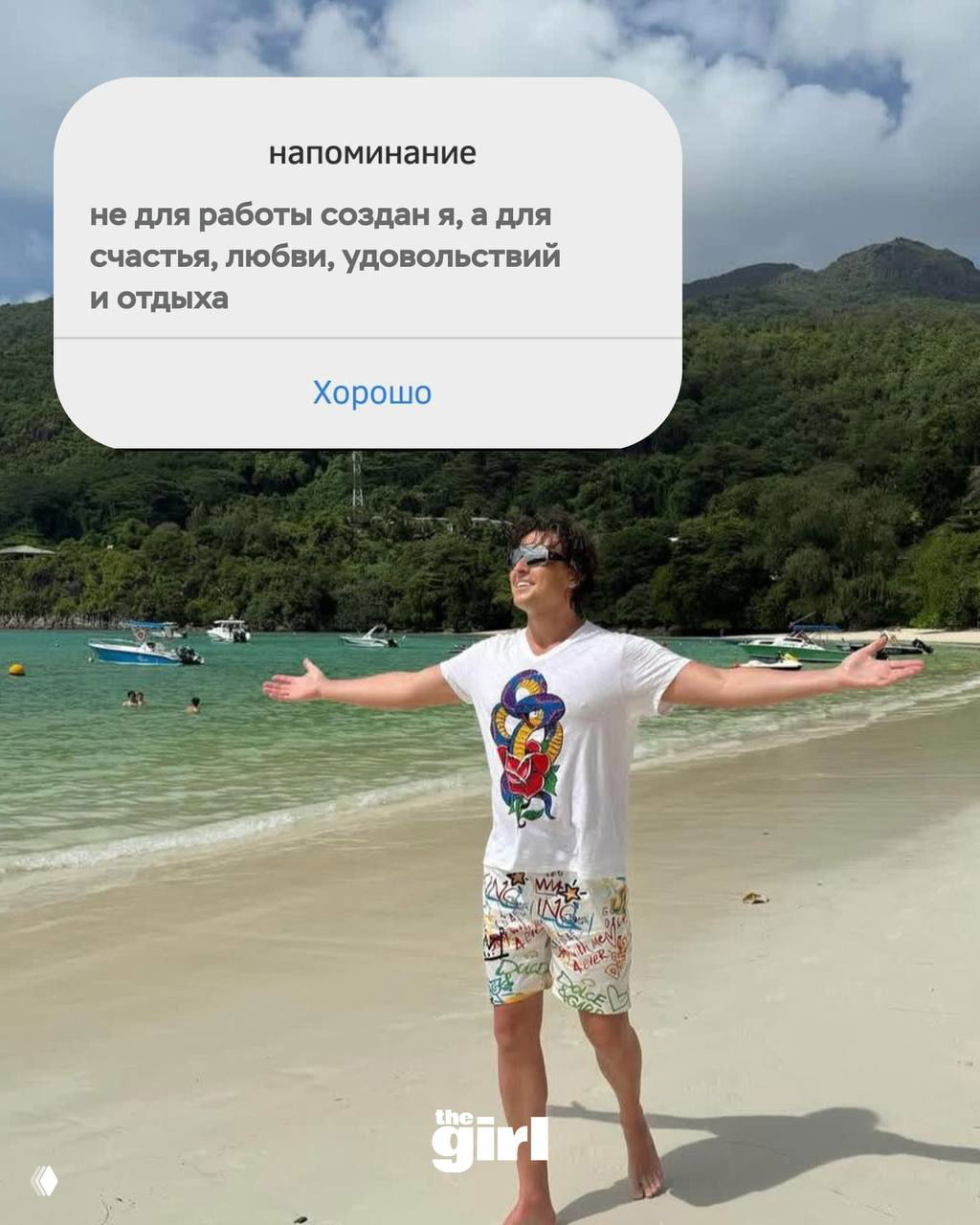 Прохор Шаляпин на пляже с раскинутыми руками: море и горы на заднем плане, поверх фото — карточка-напоминание с мотивирующей цитатой.