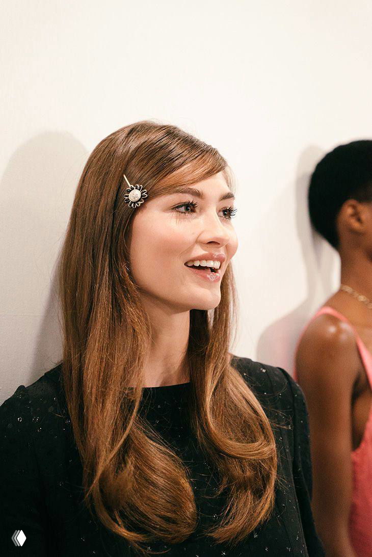 Женщина в светлом интерьере с лёгкой челкой, заколотой набок; длинные волосы и аккуратная заколка в причёске.