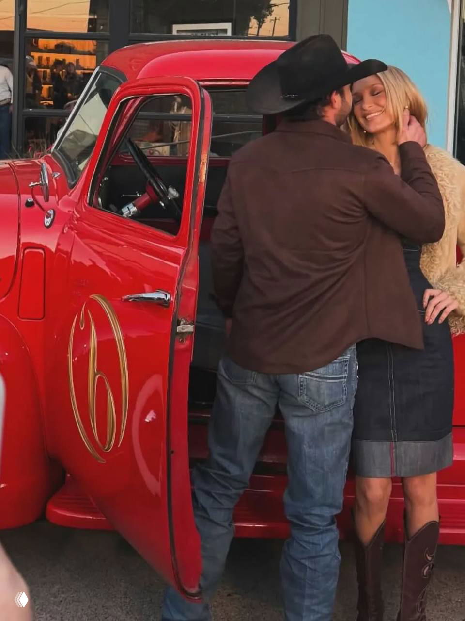 Мужчина и женщина стоят у красного авто: мужчина трогает женщину за щеку, она улыбается; кадр крупным планом.