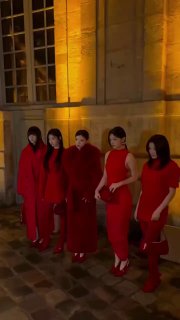 Кадр из видео: участницы ILLIT идут по коридору показа в красных платьях ночью на показе Jacquemus в Париже, короткое движущееся изображение.