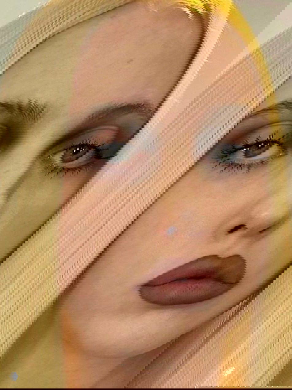 Крупный кадр лица с бледными бровями и ярко выраженными губами в коричневом блеске; эстетика 90-х через игру контраста на лице.