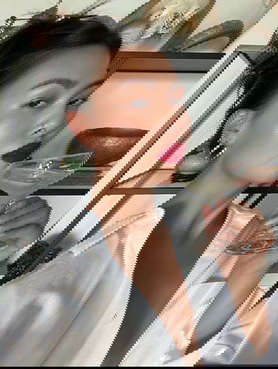 Портрет девушки со смуглой кожей и тёмными волосами, насыщенная красная помада и бокал на заднем плане, интерьер внутри комнаты.