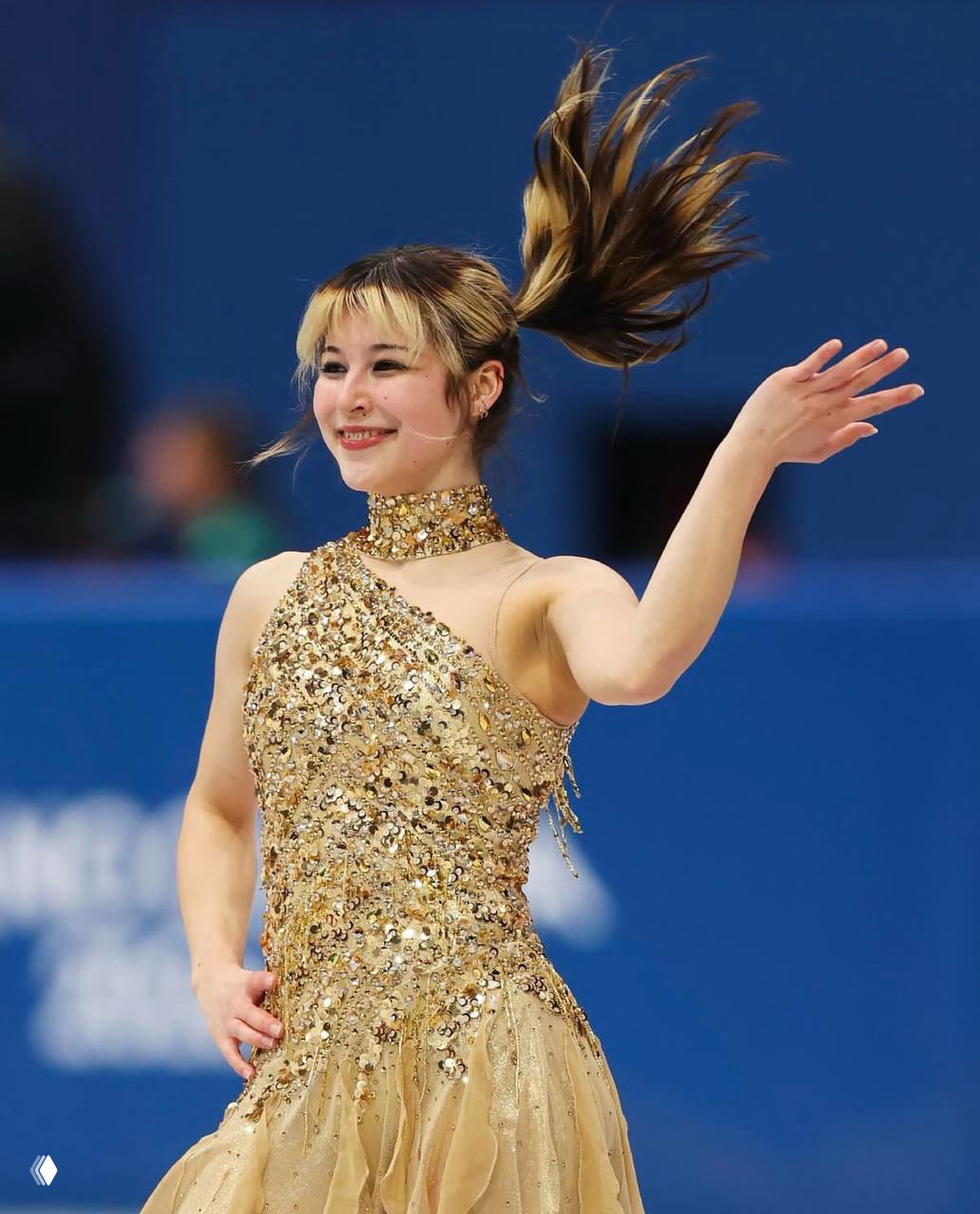 Крупный план Алисы Лью в золотистом платье: эмоции и жест после выступления на Олимпийских играх в Милане, зрительный зал размытым фоном.