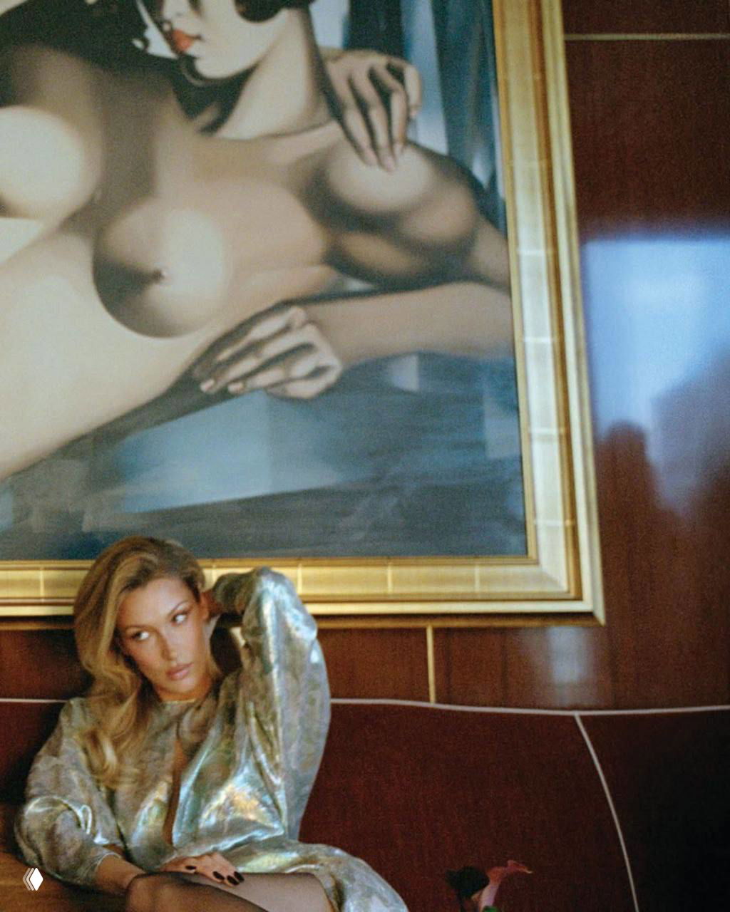 Интерьерная фотография модели на диване под крупной картиной; мягкое освещение, золотистые и бордовые оттенки в ретро‑меблировке.