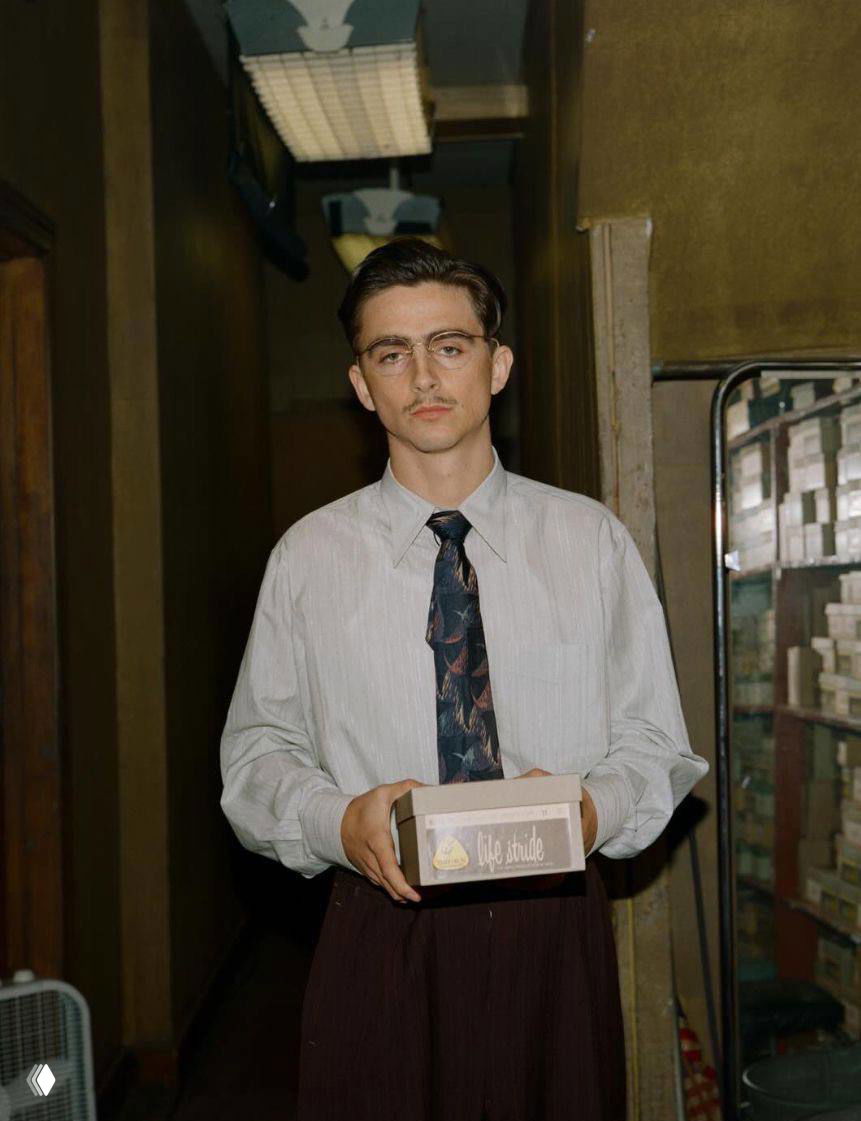 Портрет мужчины в светлой рубашке и галстуке в узком коридоре; винтажная эстетика офисного образа и спокойная тёплая палитра кадра.